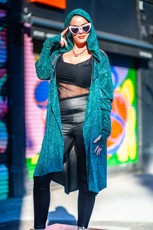 Model Amy wears the Miho cardigan with black wet look leggings, sheer top and heart sunglasses. She is stood in Manchester in front of some graffiti shutters