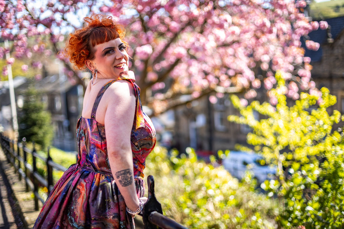 Lindsey with red hair and wearing a swing dress, standing in a park with cherry blossoms in the background
