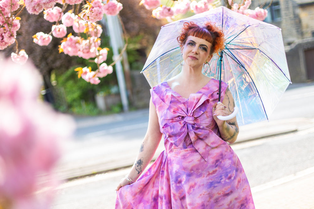 Lindsey in a pink dress holding a transparent umbrella with cherry blossoms in the background